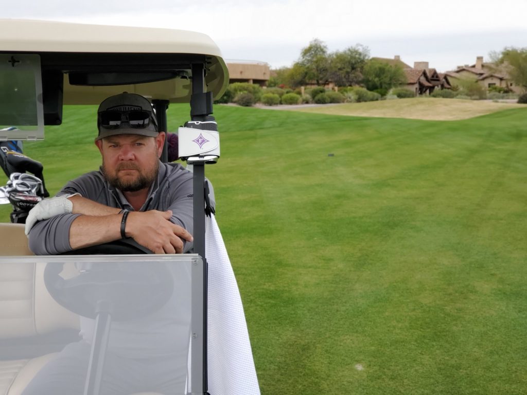 Man in a golf cart on a lush, green course, wearing a gray shirt, ready for a day of golfing.