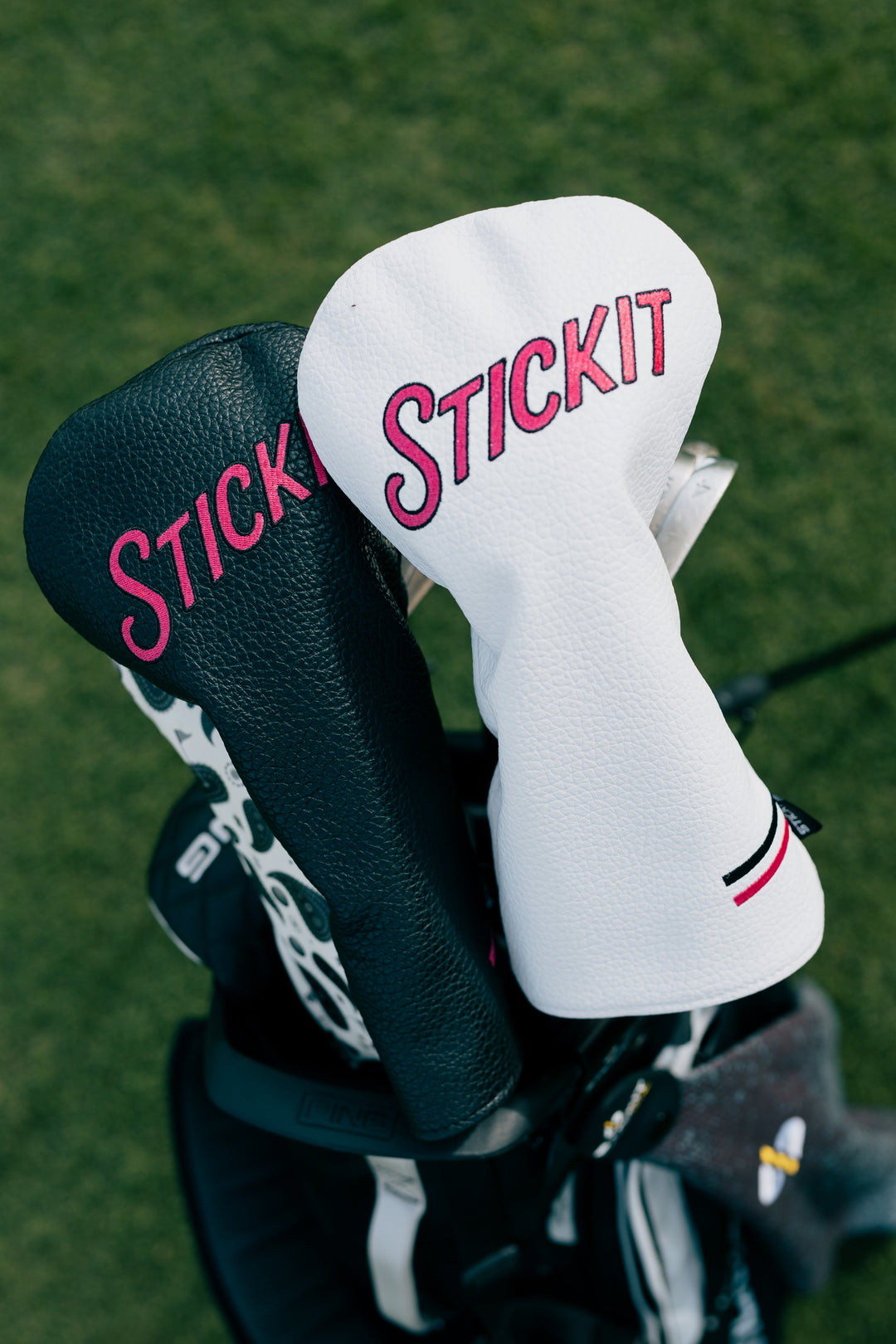 Black and white golf headcovers with "STICKIT" in pink, stylish leather design for a modern golf look.