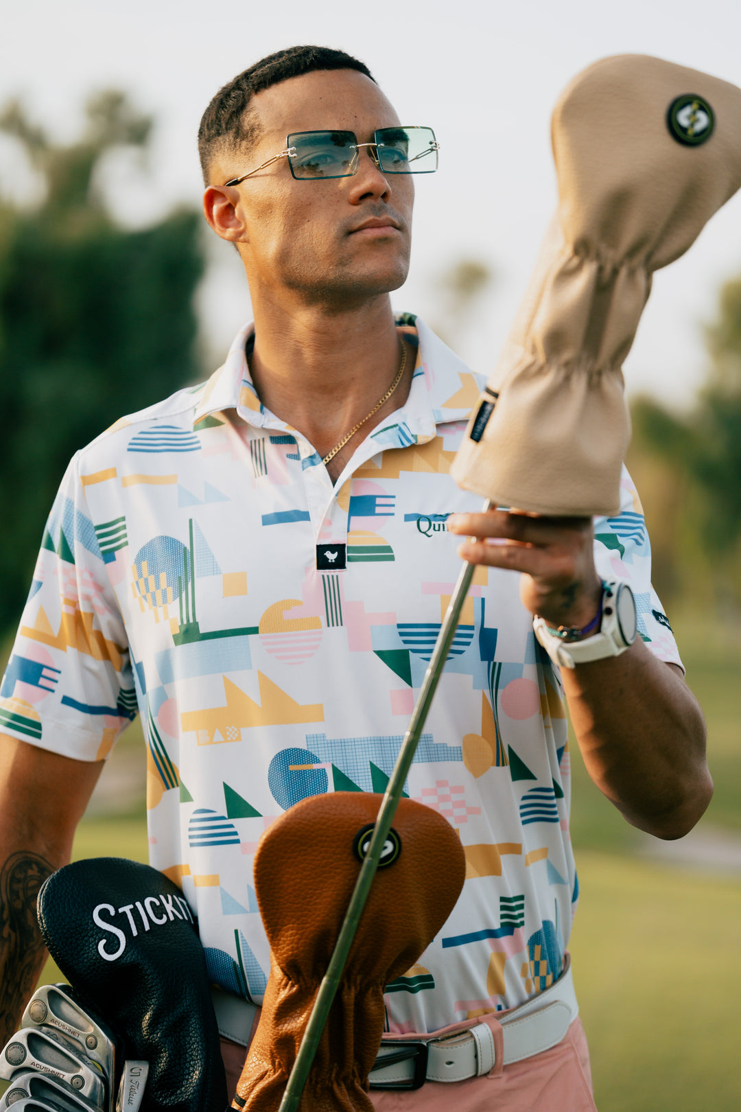Men's colorful patterned golf polo, featuring pastel shades, paired with stylish sunglasses and golf club covers.