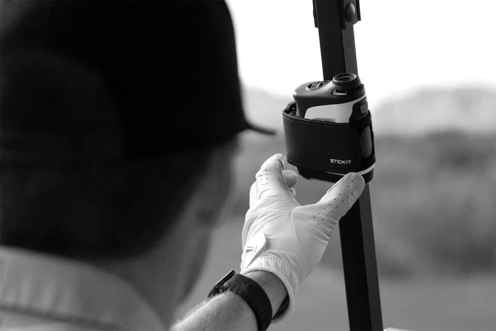 White golf glove adjusting a black StickIt golf accessory holder, mounted on a golf cart. Perfect for easy access on the course.