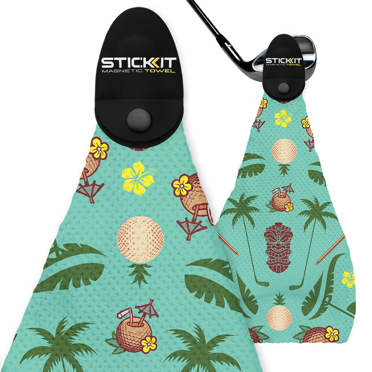 Tropical-themed magnetic golf towel with mint green background, featuring golf balls, tiki masks, and palm leaves.