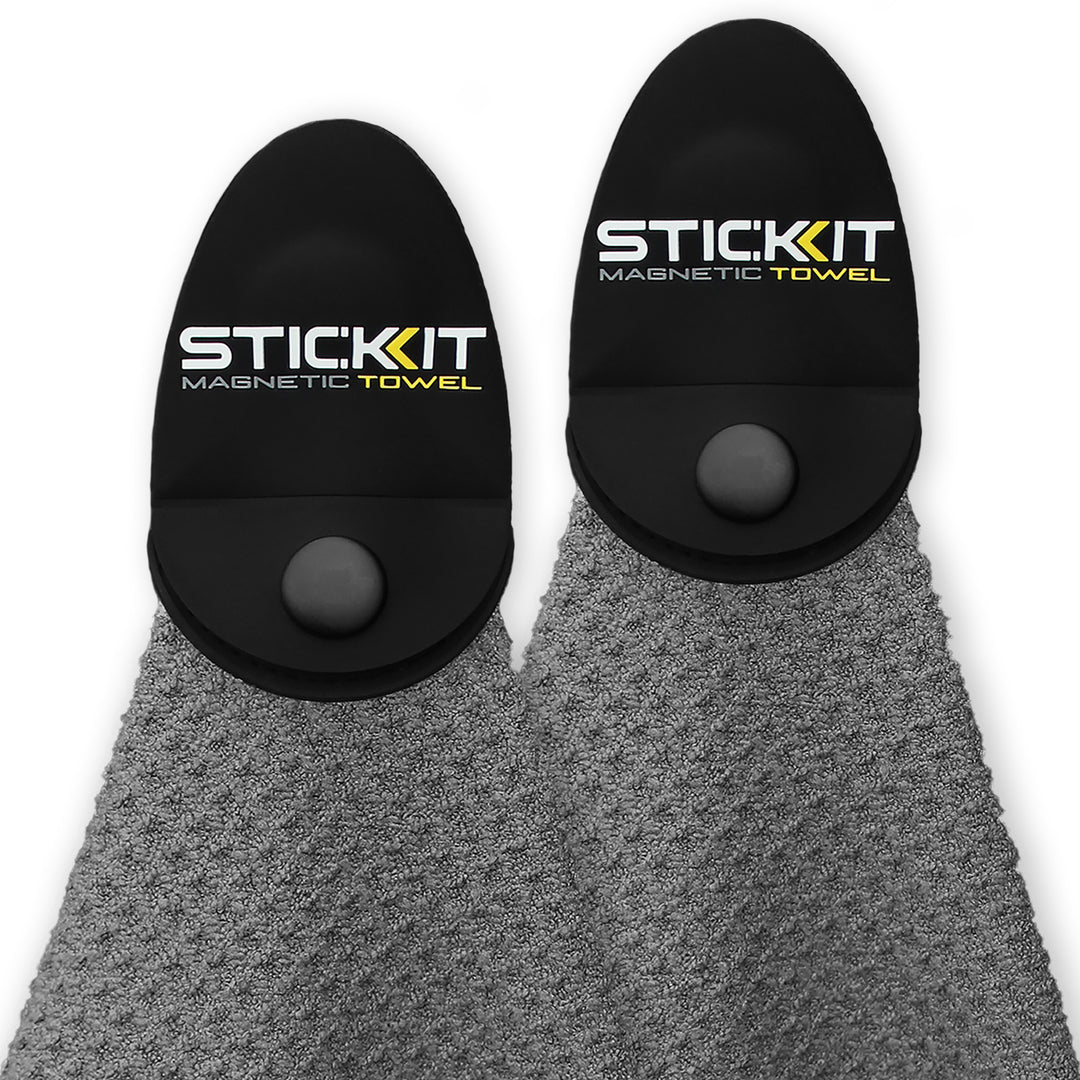 Gray textured towel with black magnetic holder, branded "STICKIT," perfect for workouts and outdoor activities.