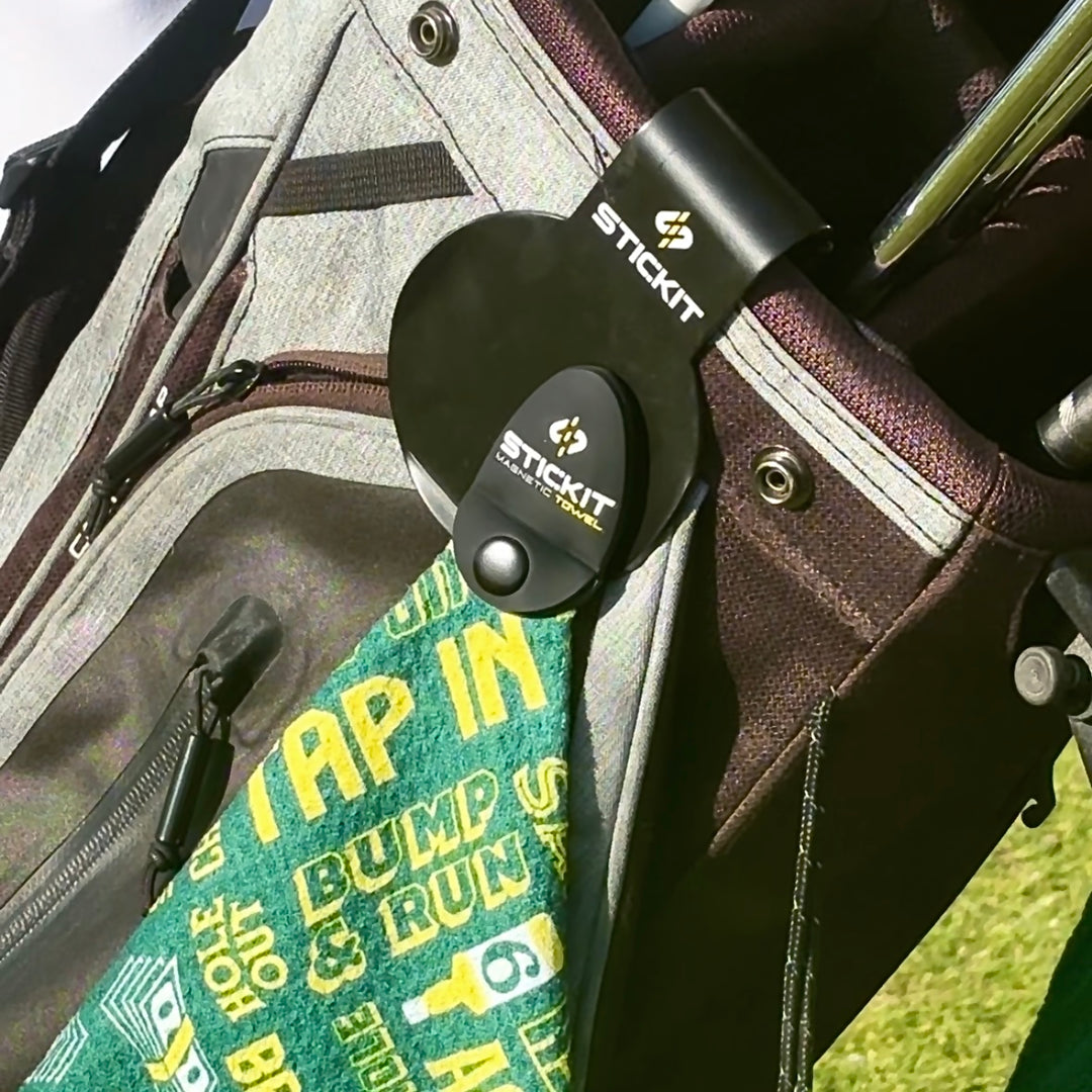 Black golf towel clip on a gray golf bag, featuring green towel with yellow text "TAP IN BUMP N RUN".