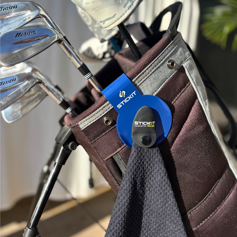 Blue StickIt golf towel clip, with dark brown golf bag, holding golf clubs. Durable, stylish accessory for golfers.
