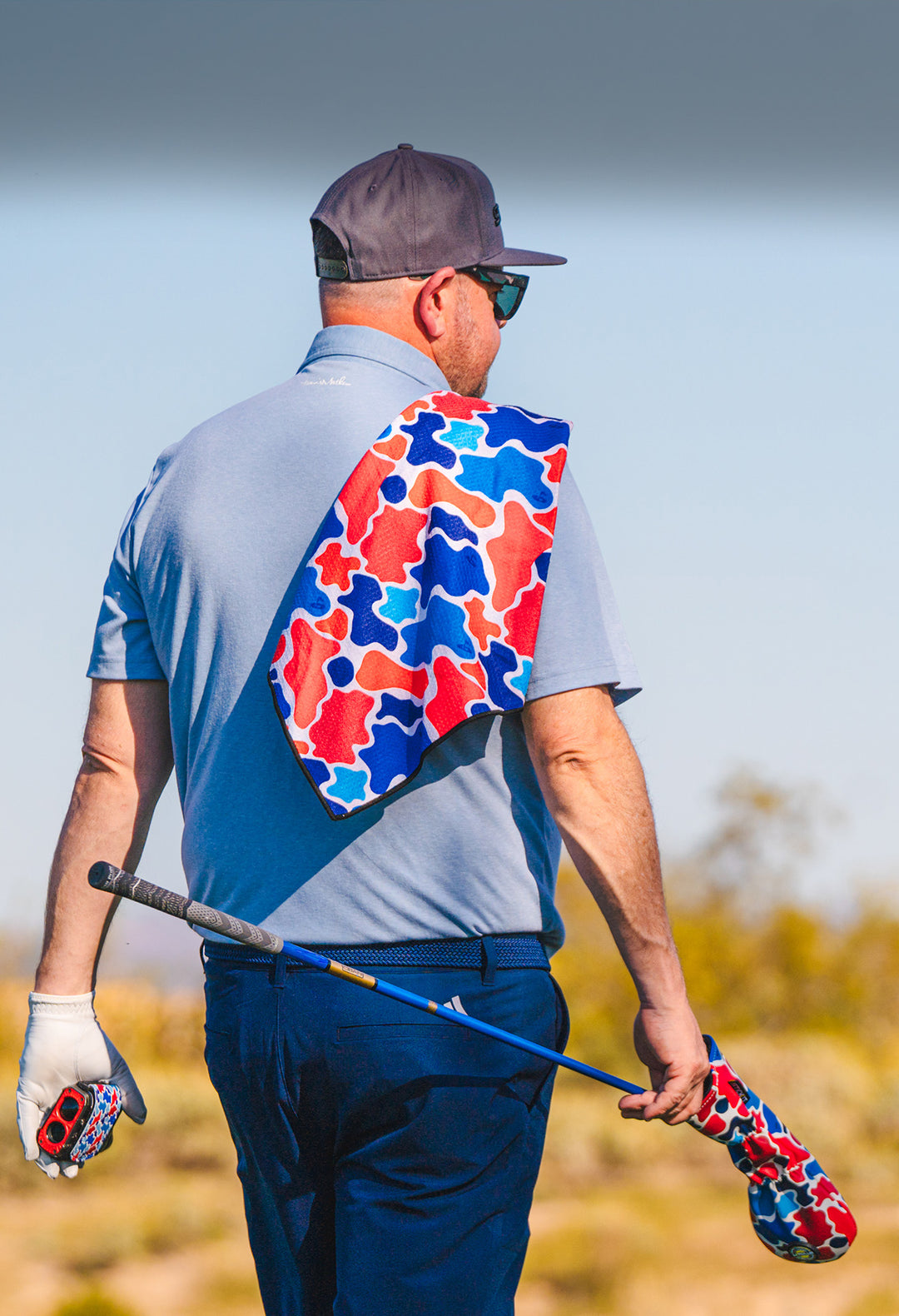 Men's golf outfit featuring a light blue polo, red and blue camo-patterned towel, and matching club covers.