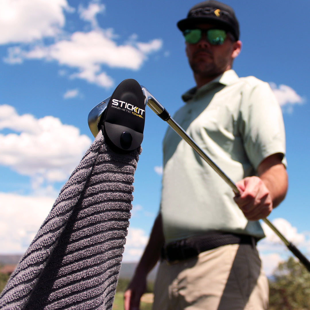 STICKIT golf towel, gray microfiber with clip, perfect for golfers, showcased outdoors on a sunny day.