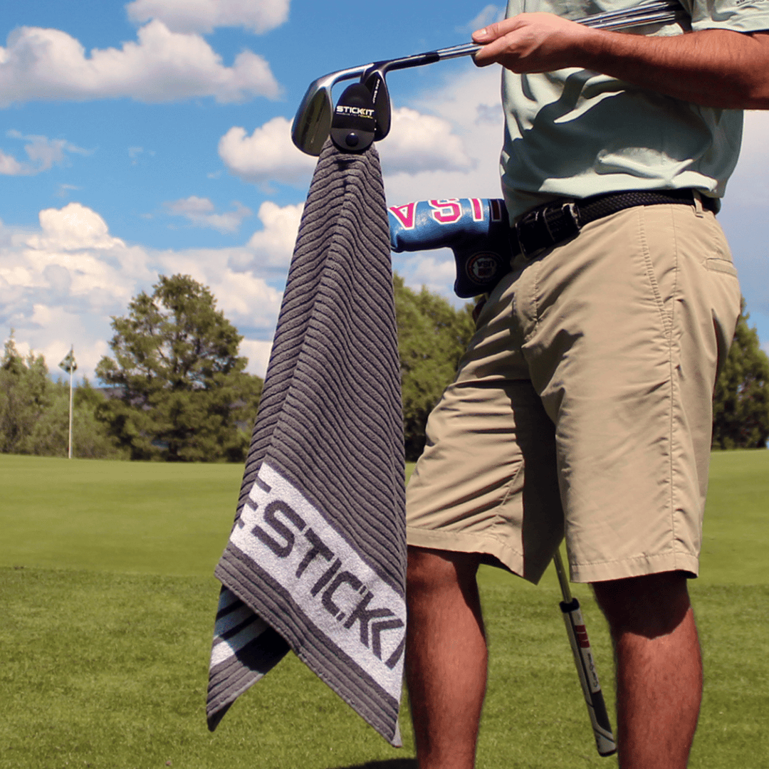 Men's golf towel in gray with vibrant blue accents, held by a golfer on a lush green course.